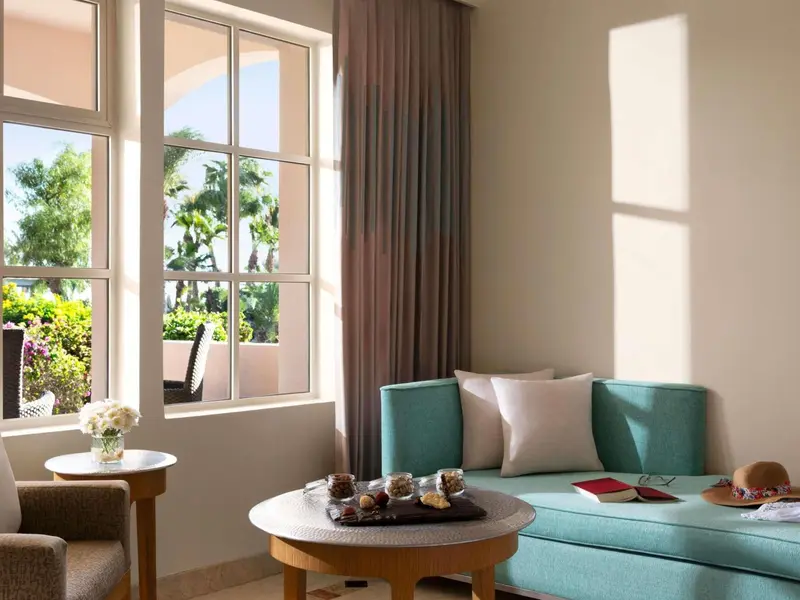 Un canapé turquoise et une table basse ornent un espace de détente lumineux avec vue sur la végétation.