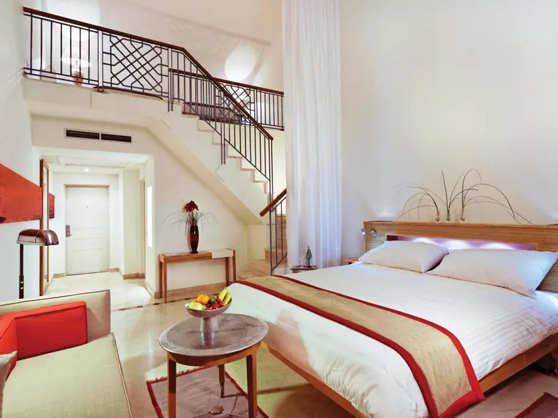 Une chambre lumineuse avec un lit double et un escalier menant à une mezzanine.