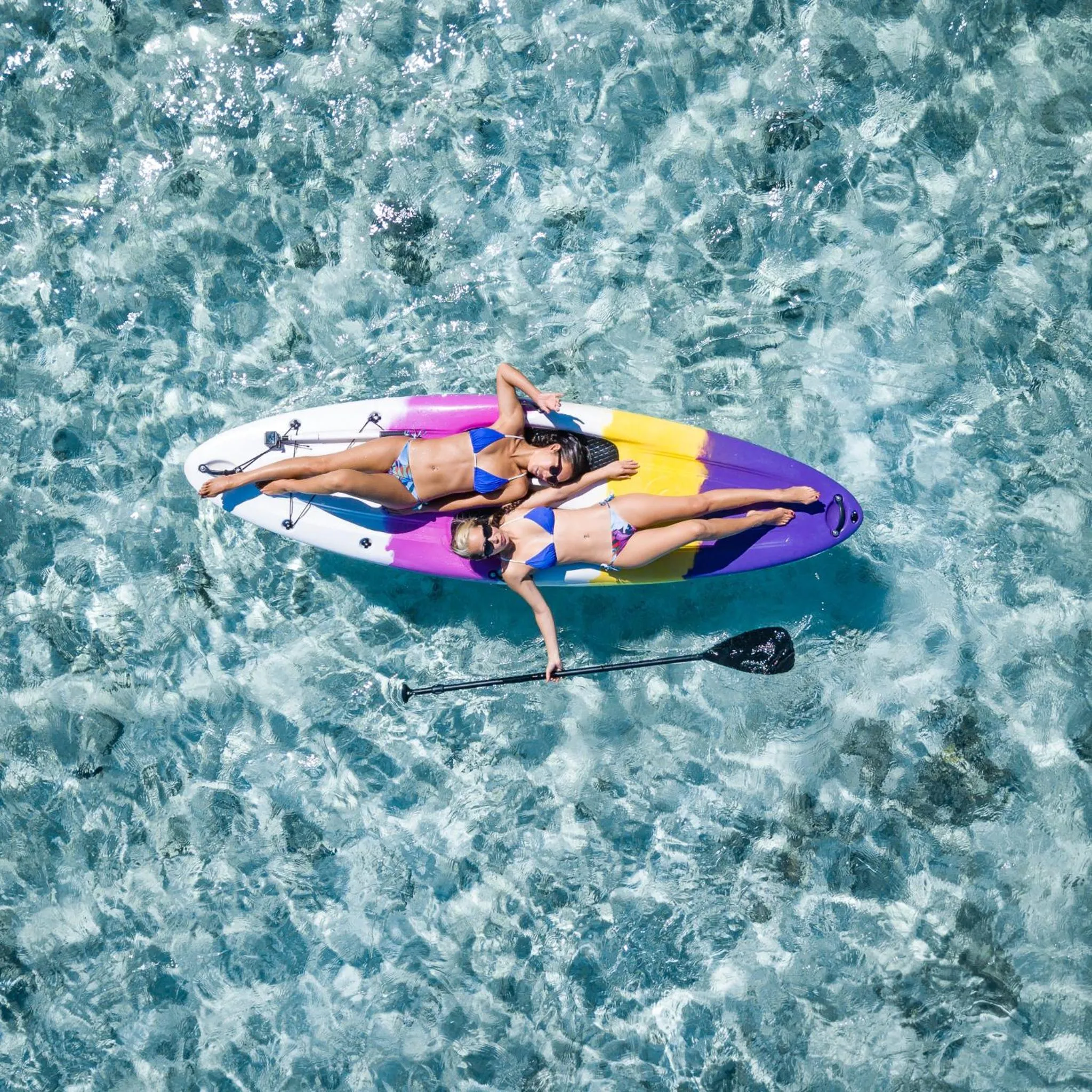 Deux personnes se détendent sur une planche de paddle dans une eau turquoise.