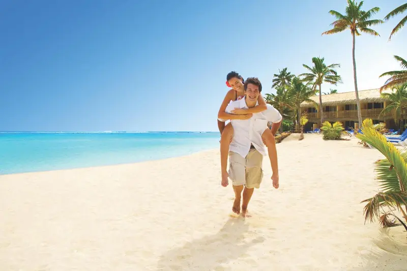 Un couple marche sur une plage de sable blanc bordée de palmiers.