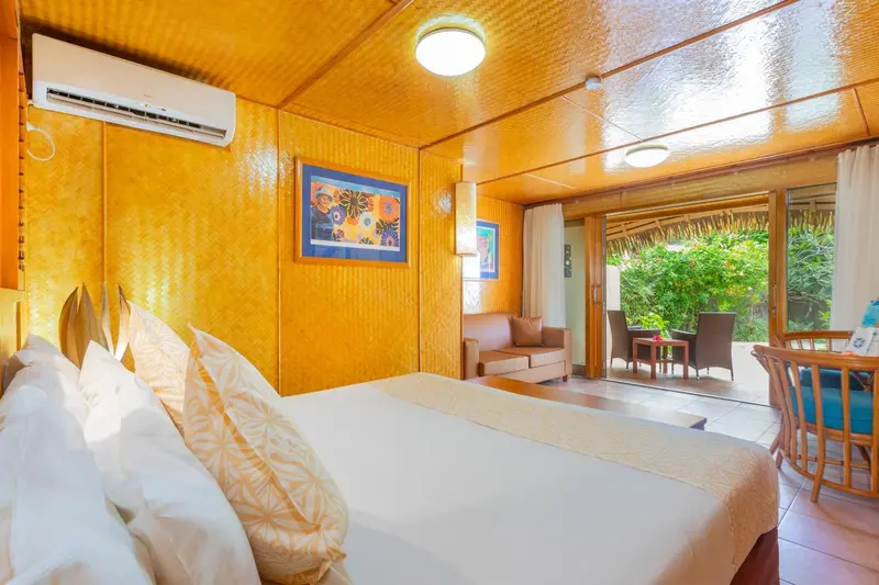 Une chambre lumineuse avec un lit fait et un coin salon ouvert sur l'extérieur.
