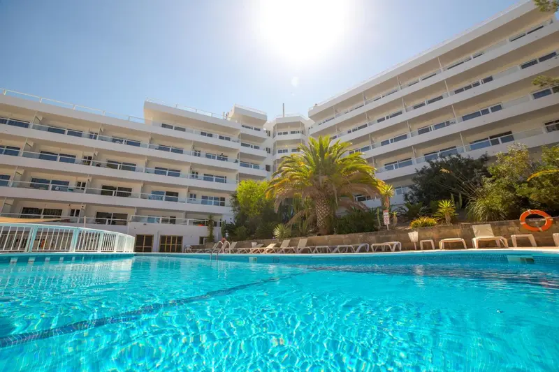 Vue d'un bâtiment blanc avec des balcons surplombant une piscine bleu clair.