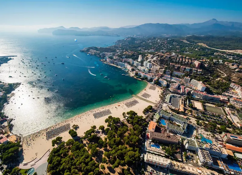 Vue aérienne d'une station balnéaire avec une plage de sable fin et des bâtiments blancs.