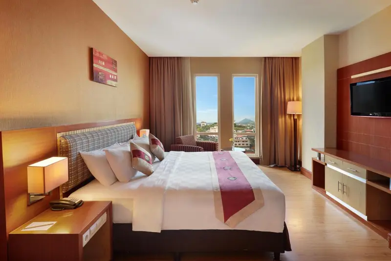 Chambre lumineuse avec un grand lit et une vue sur la ville.