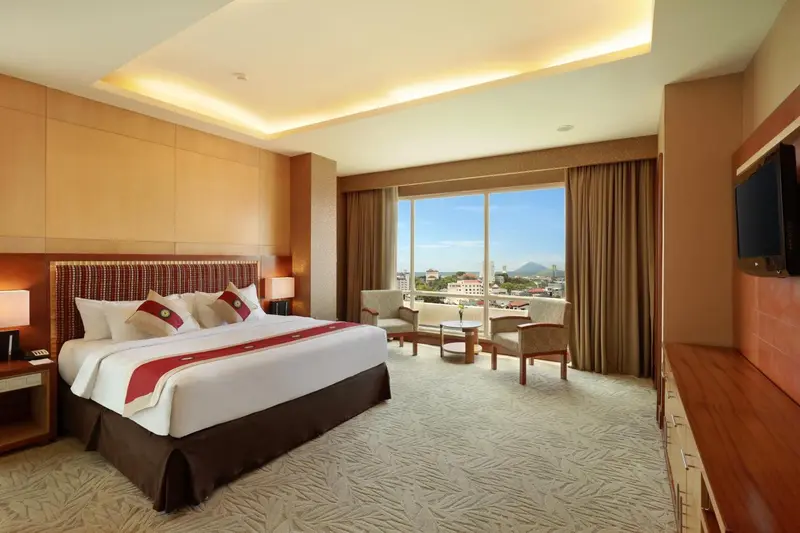 Chambre lumineuse avec un grand lit et un coin salon près d'une fenêtre.