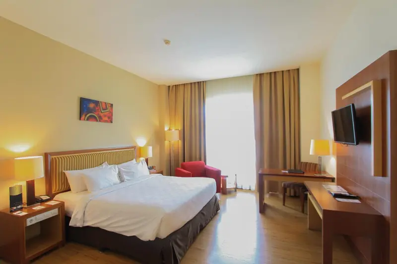 Une chambre lumineuse avec un grand lit et un fauteuil rouge.