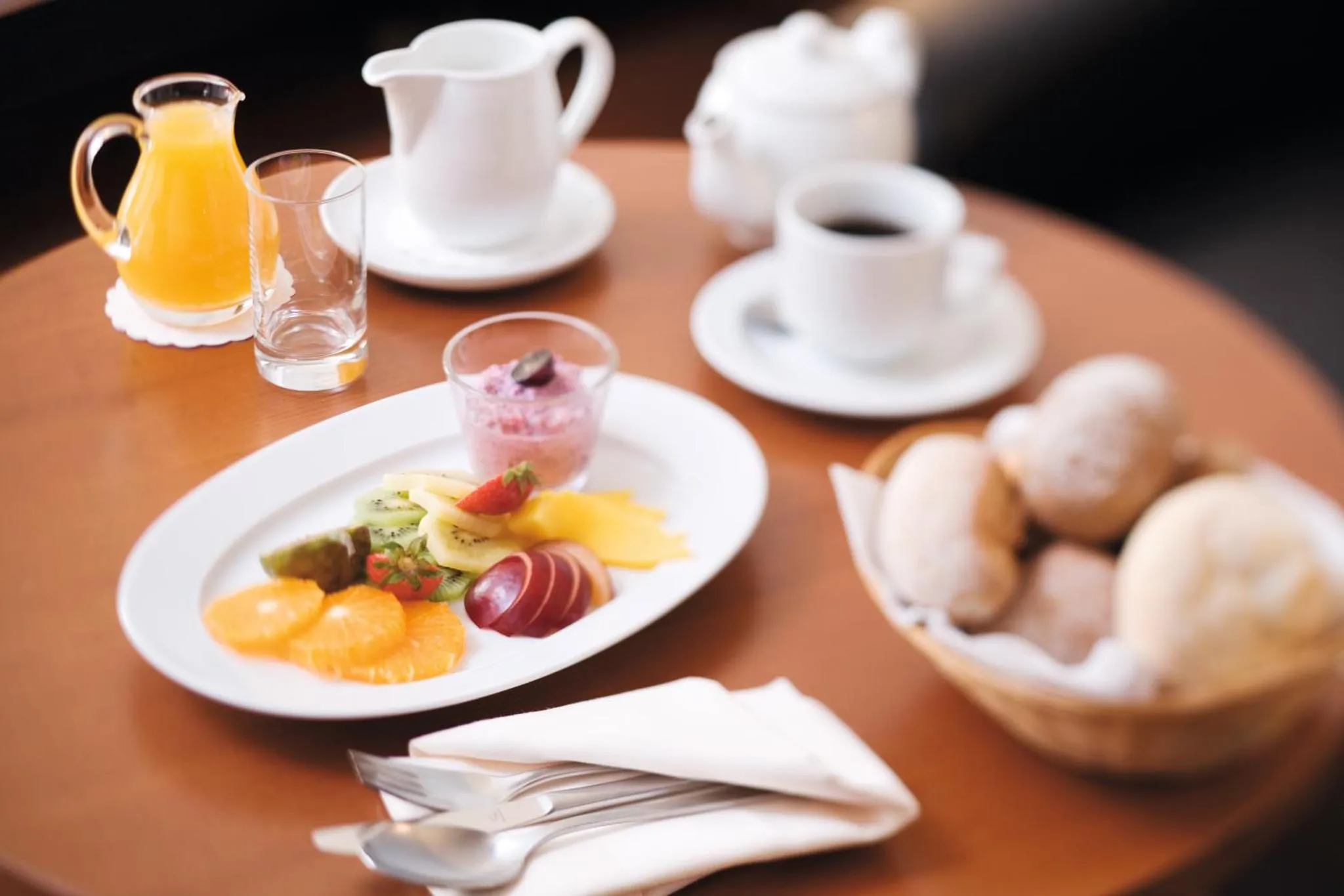 Une table ronde présente un petit-déjeuner avec des fruits frais, des viennoiseries et des boissons.