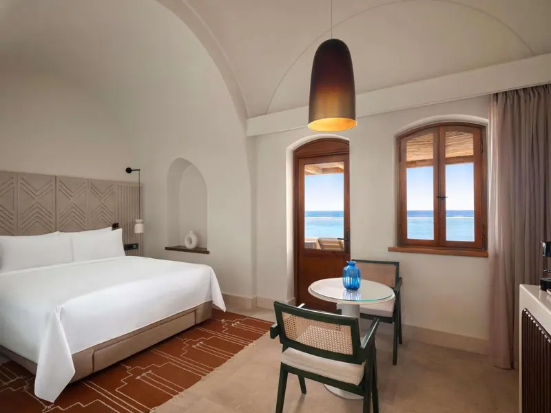 Chambre lumineuse avec un grand lit et une vue sur la mer.