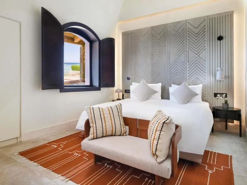 Une chambre lumineuse avec un grand lit et une fenêtre ouverte sur la mer.