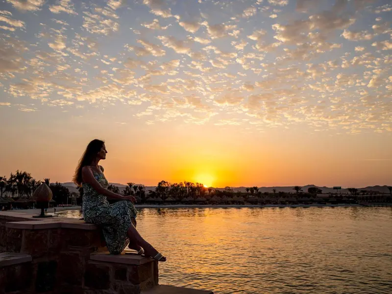 Une femme assise au bord de l'eau admire un coucher de soleil flamboyant.