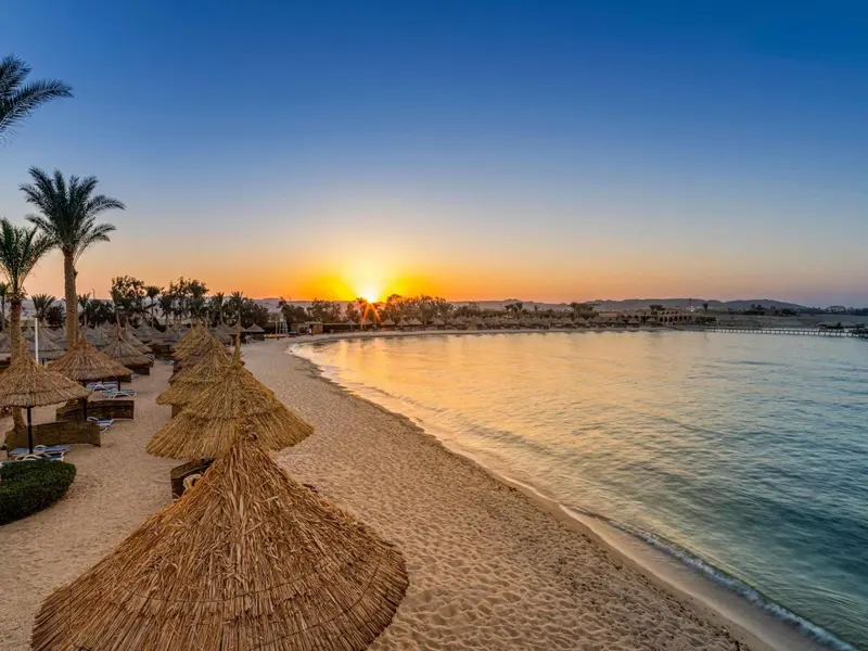 Plage de sable fin avec parasols en chaume au coucher du soleil.