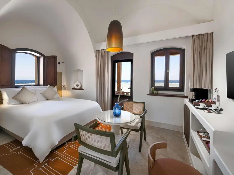 Une chambre lumineuse avec un lit blanc et une table ronde près d'une fenêtre.