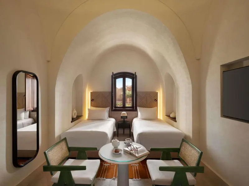 Une chambre lumineuse avec deux lits simples et une fenêtre cintrée.