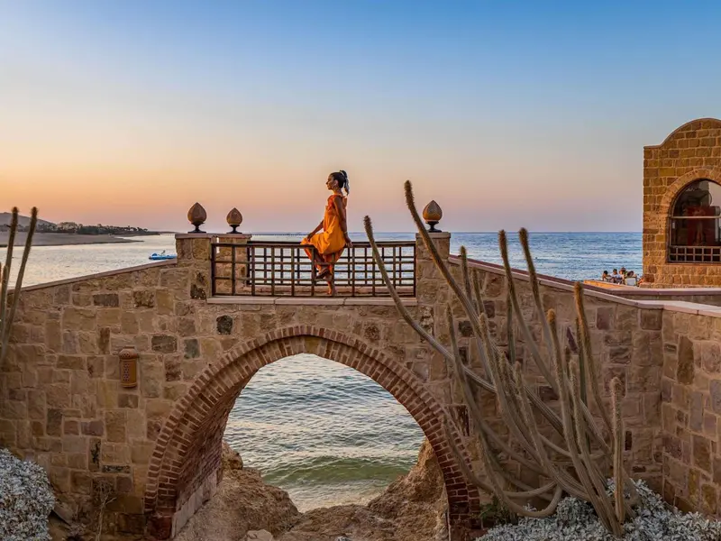 Une personne assise sur un pont en pierre surplombe la mer au coucher du soleil.