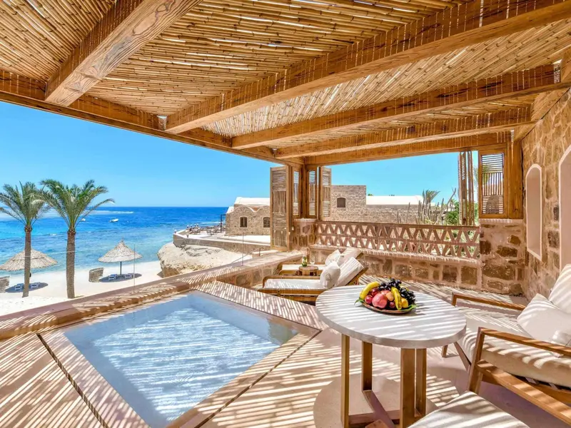 Terrasse ombragée avec jacuzzi et table garnie de fruits frais, vue sur la mer.