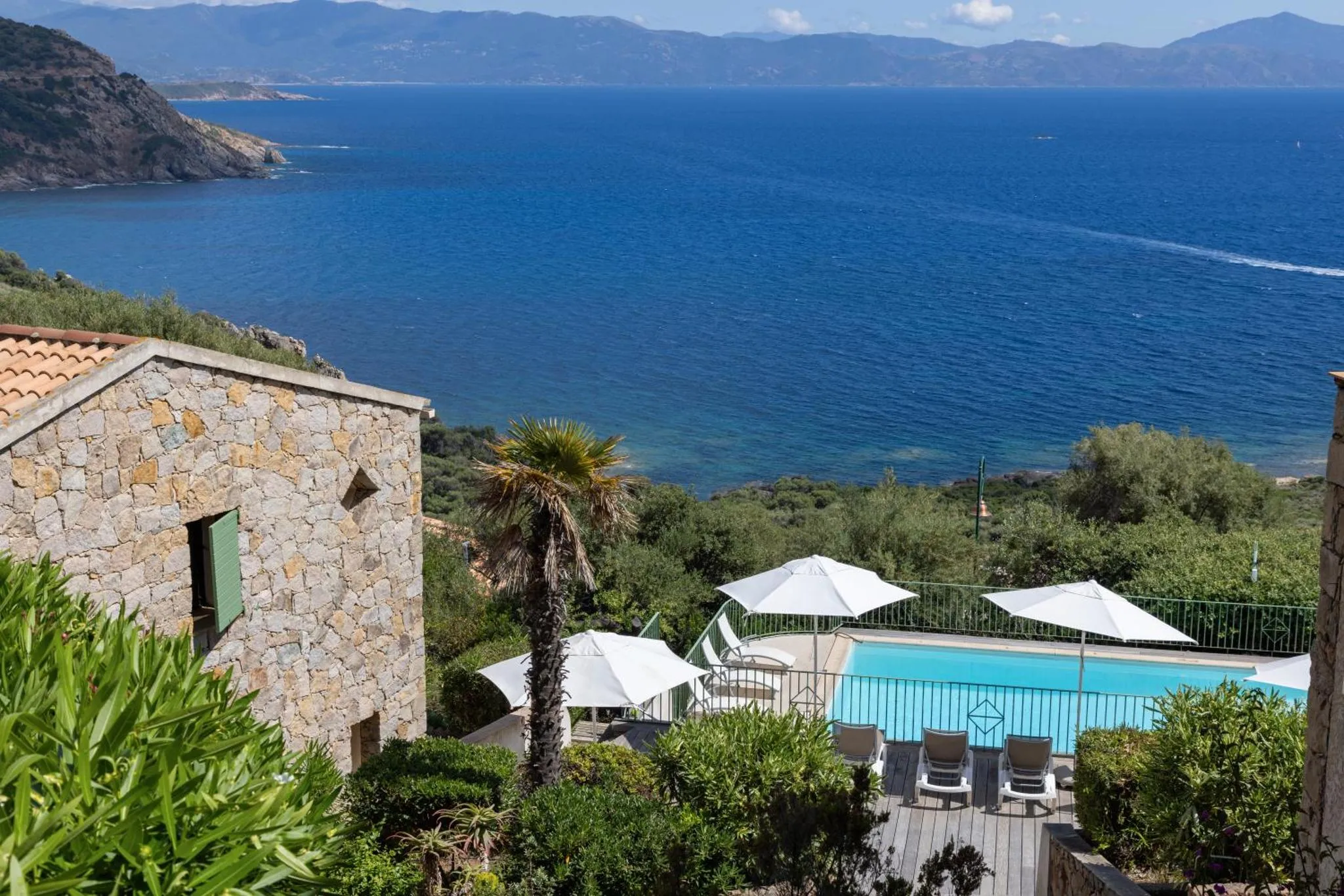 Vue d'une piscine et d'une terrasse avec transats surplombant la mer.