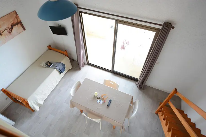 Une chambre avec un lit simple et une table à manger près d'une baie vitrée.