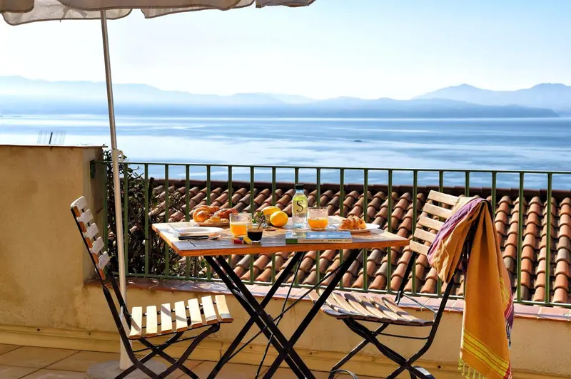 Une table de petit-déjeuner est dressée sur une terrasse avec vue sur la mer et les montagnes.