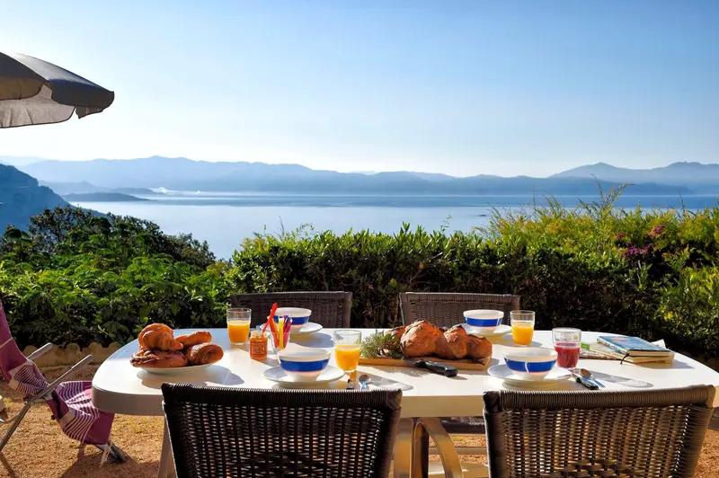Une table de petit-déjeuner est dressée sur une terrasse avec vue sur la mer et les montagnes.