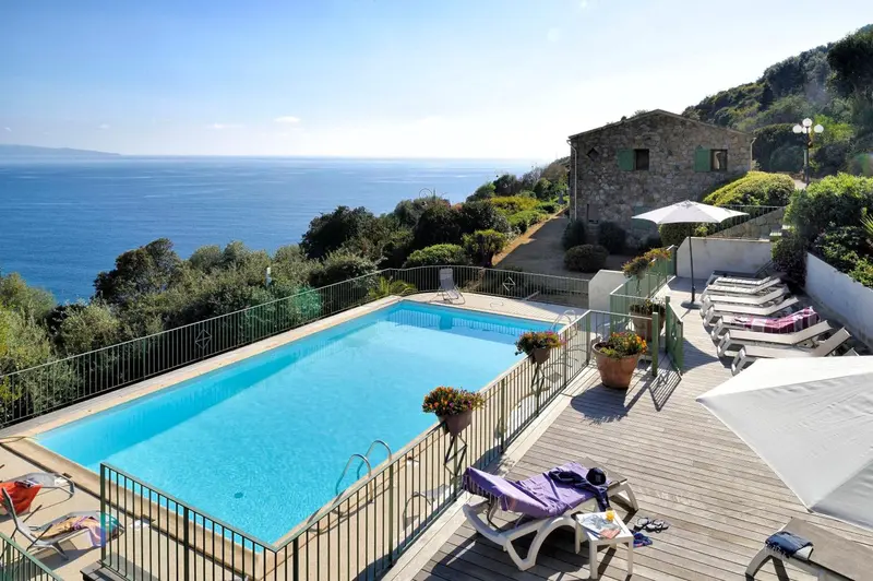 Une piscine turquoise bordée d'une terrasse ensoleillée avec chaises longues et vue sur la mer.
