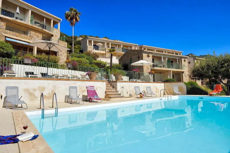 Terrasse ensoleillée avec chaises longues et piscine bleue au premier plan.