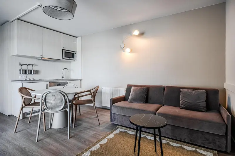 Espace de vie avec cuisine équipée et canapé gris.
