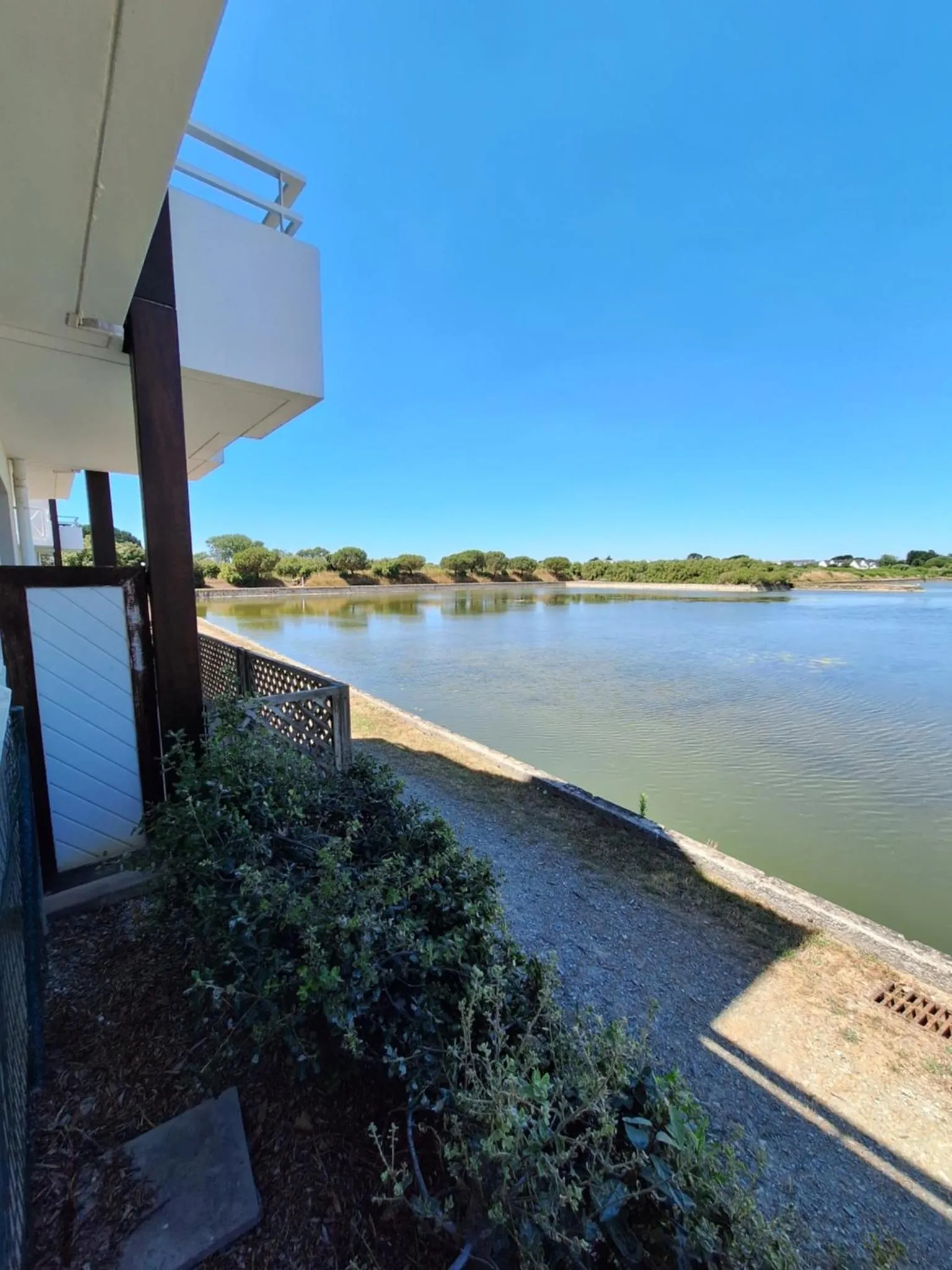 Vue sur un plan d'eau depuis une terrasse ombragée.