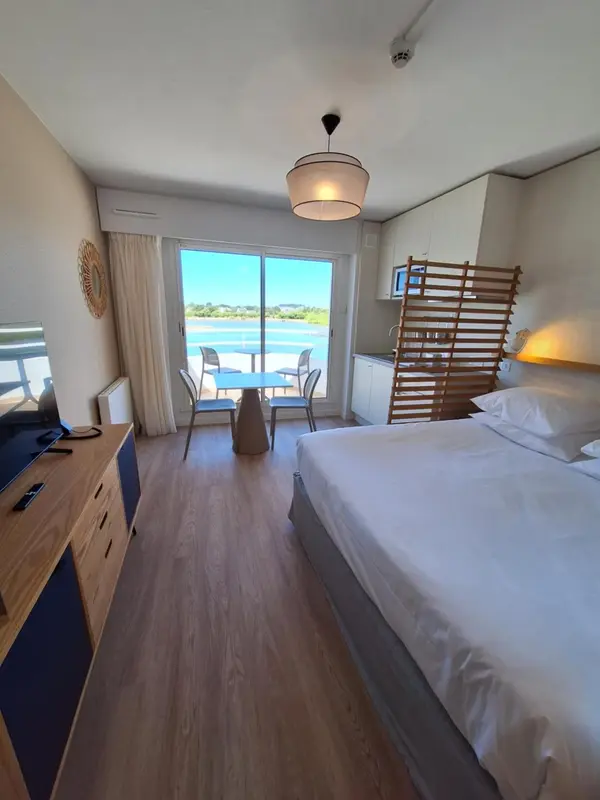 Chambre lumineuse avec un lit fait et un coin repas près d'une baie vitrée.