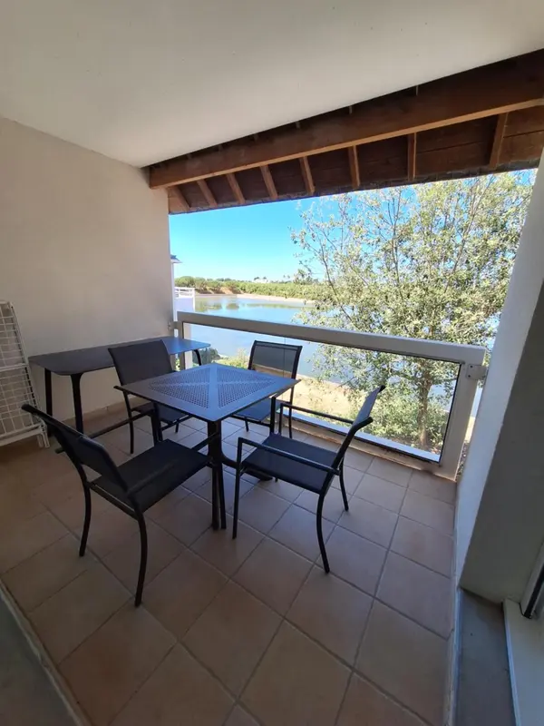 Terrasse carrelée avec table et chaises donnant sur un paysage aquatique.