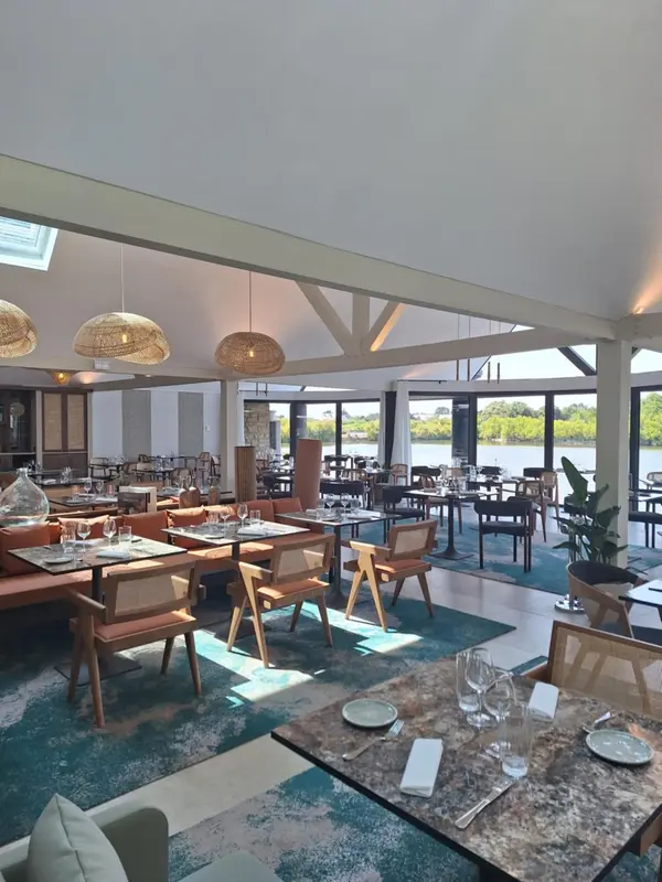 Une salle de restaurant lumineuse avec des tables dressées et une vue sur l'eau.