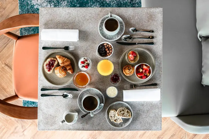Une table est dressée pour le petit-déjeuner avec des viennoiseries, des fruits et des boissons.