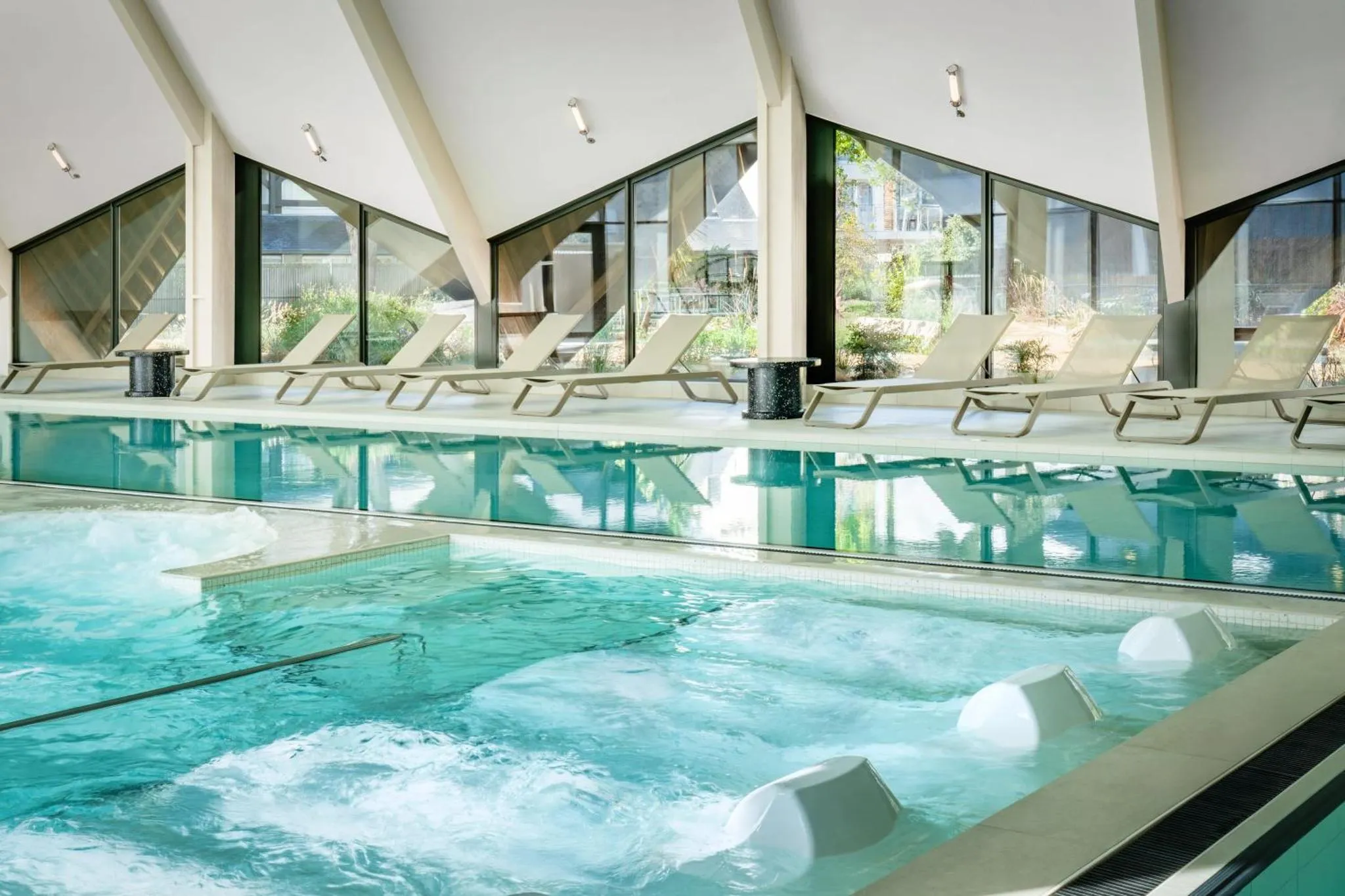 Une piscine intérieure lumineuse avec des transats alignés devant de grandes baies vitrées.