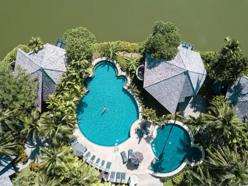 Vue aérienne d'un complexe hôtelier avec des piscines et une végétation luxuriante.