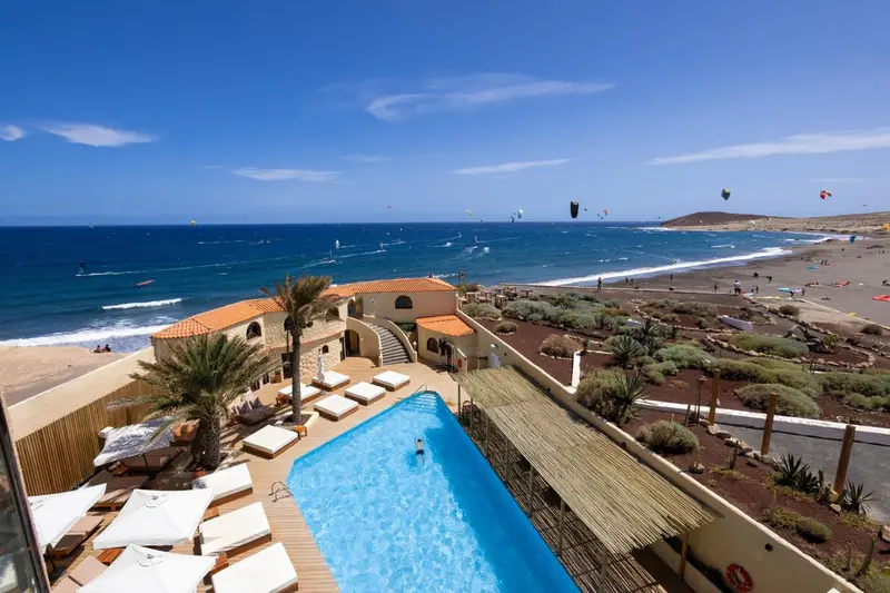 Vue aérienne d'une piscine d'hôtel avec des transats et la mer en arrière-plan.