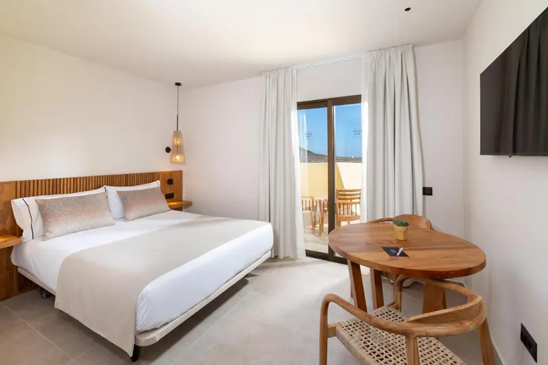 Une chambre lumineuse avec un grand lit et une table à manger près d'une baie vitrée.