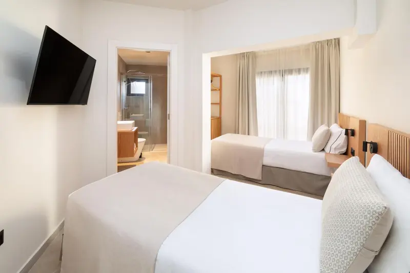 Une chambre lumineuse avec deux lits simples et un accès à une salle de bain.