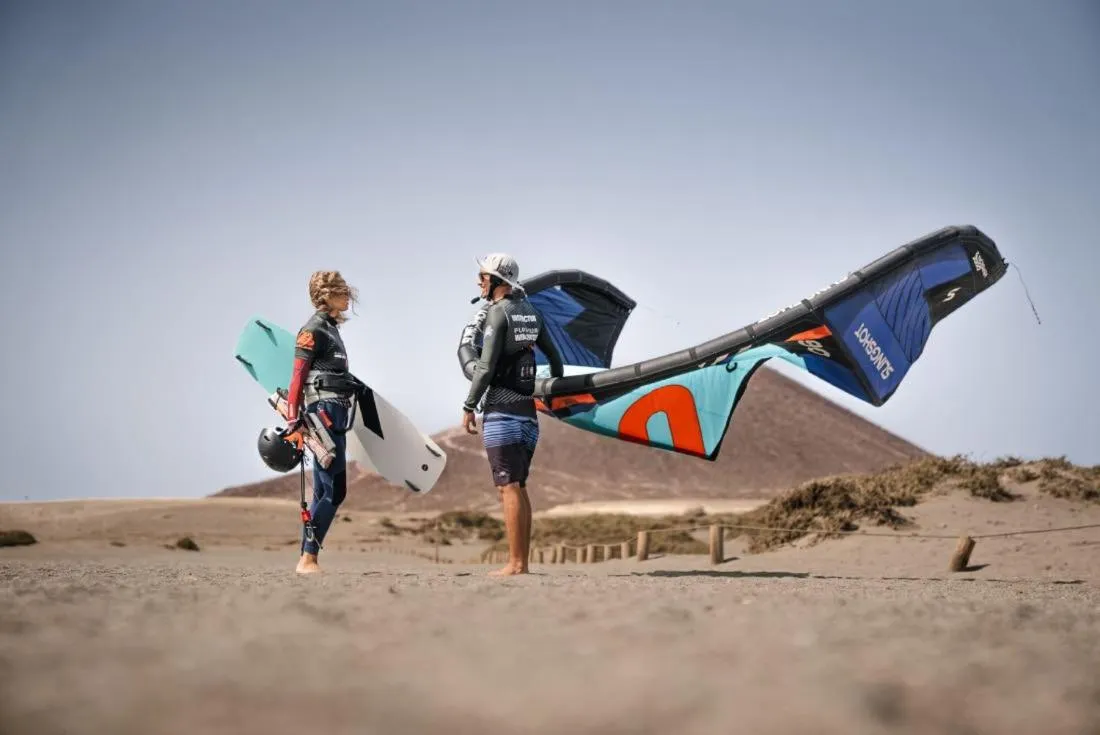 Deux personnes se tiennent sur une plage de sable avec du matériel de kitesurf.