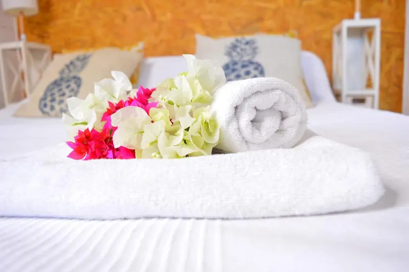 Un lit recouvert de draps blancs est décoré de fleurs et de serviettes enroulées.