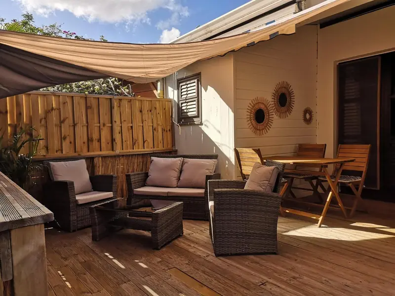 Espace extérieur aménagé avec salon de jardin et table à manger sous auvent.