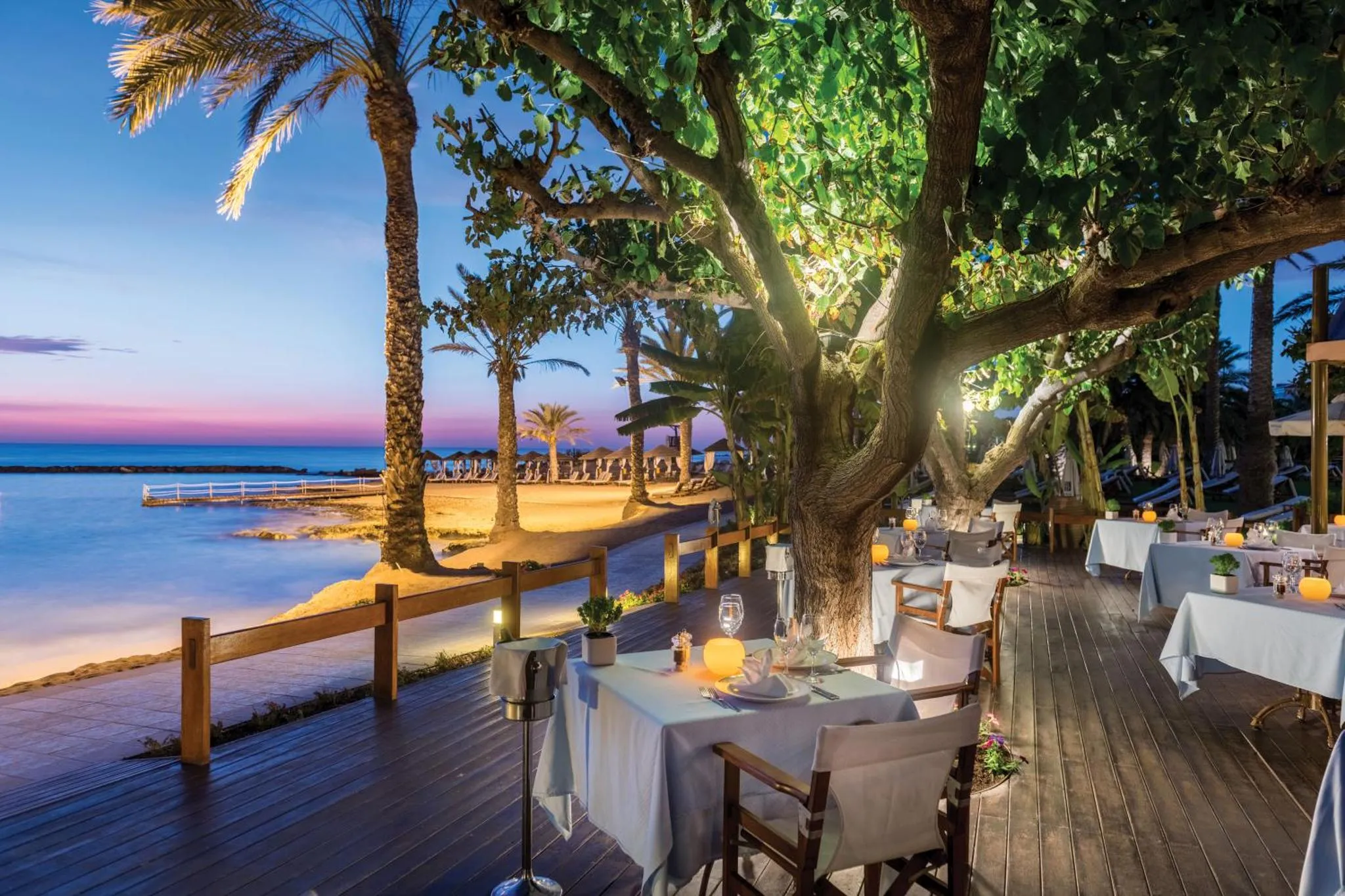 Tables dressées en terrasse au bord de la mer au coucher du soleil.