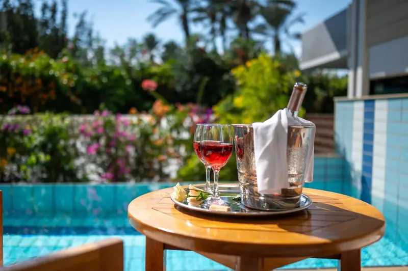 Une table basse avec une bouteille, deux verres et un seau à glace près d'une piscine.