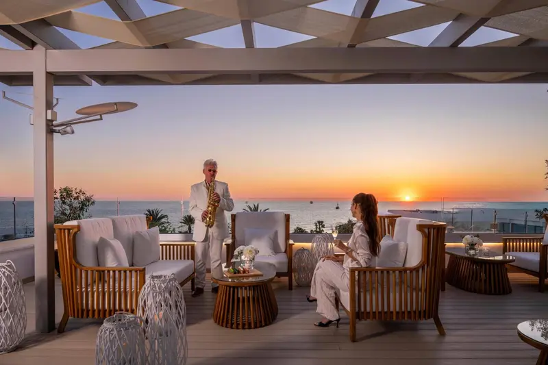 Un musicien joue du saxophone sur une terrasse avec vue sur la mer au coucher du soleil.