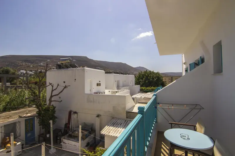 Vue d'une terrasse avec table et chaises donnant sur des bâtiments blancs et des collines.