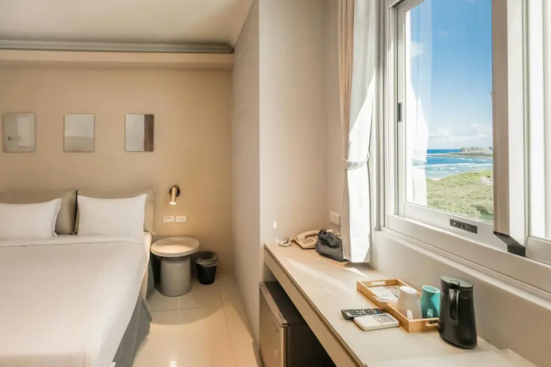Une chambre lumineuse avec un lit fait et une vue sur la mer par la fenêtre.