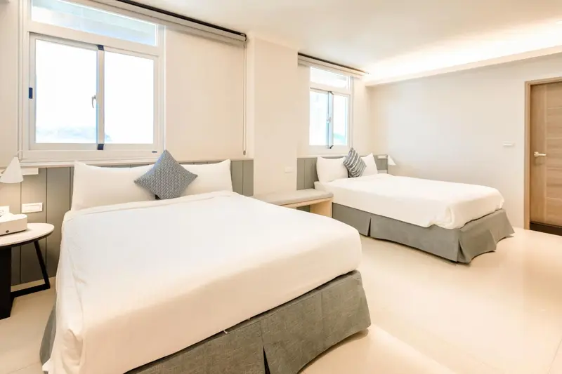 Chambre lumineuse avec deux lits doubles et une fenêtre.