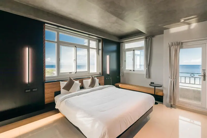 Une chambre lumineuse avec un grand lit face à une baie vitrée donnant sur la mer.
