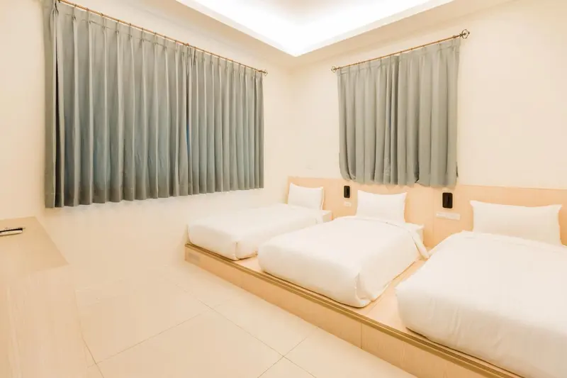 Une chambre lumineuse avec trois lits simples et des rideaux gris.