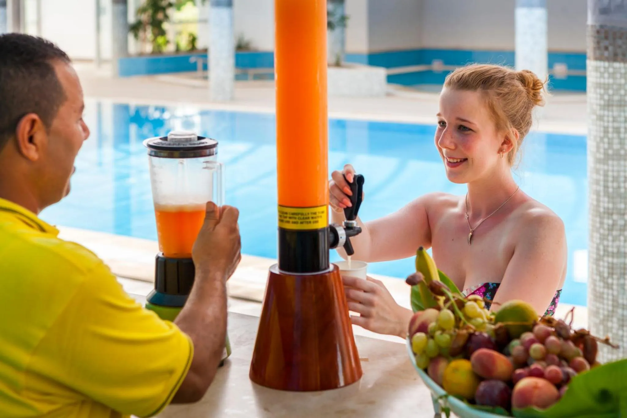 Deux personnes sourient en sirotant des boissons au bord d'une piscine.