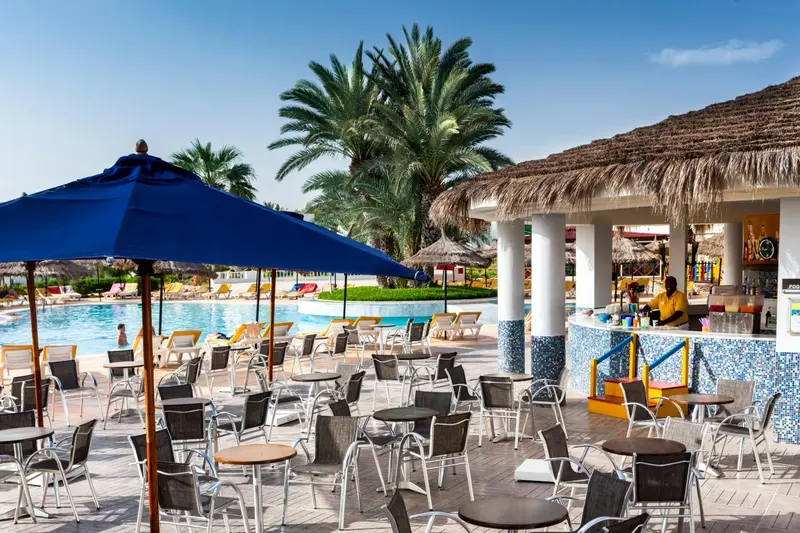 Un bar en bord de piscine avec des transats et des parasols bleus.