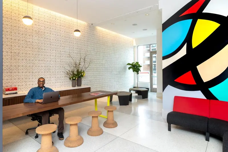 Un homme est assis à un bureau dans un espace lumineux avec une décoration murale colorée.